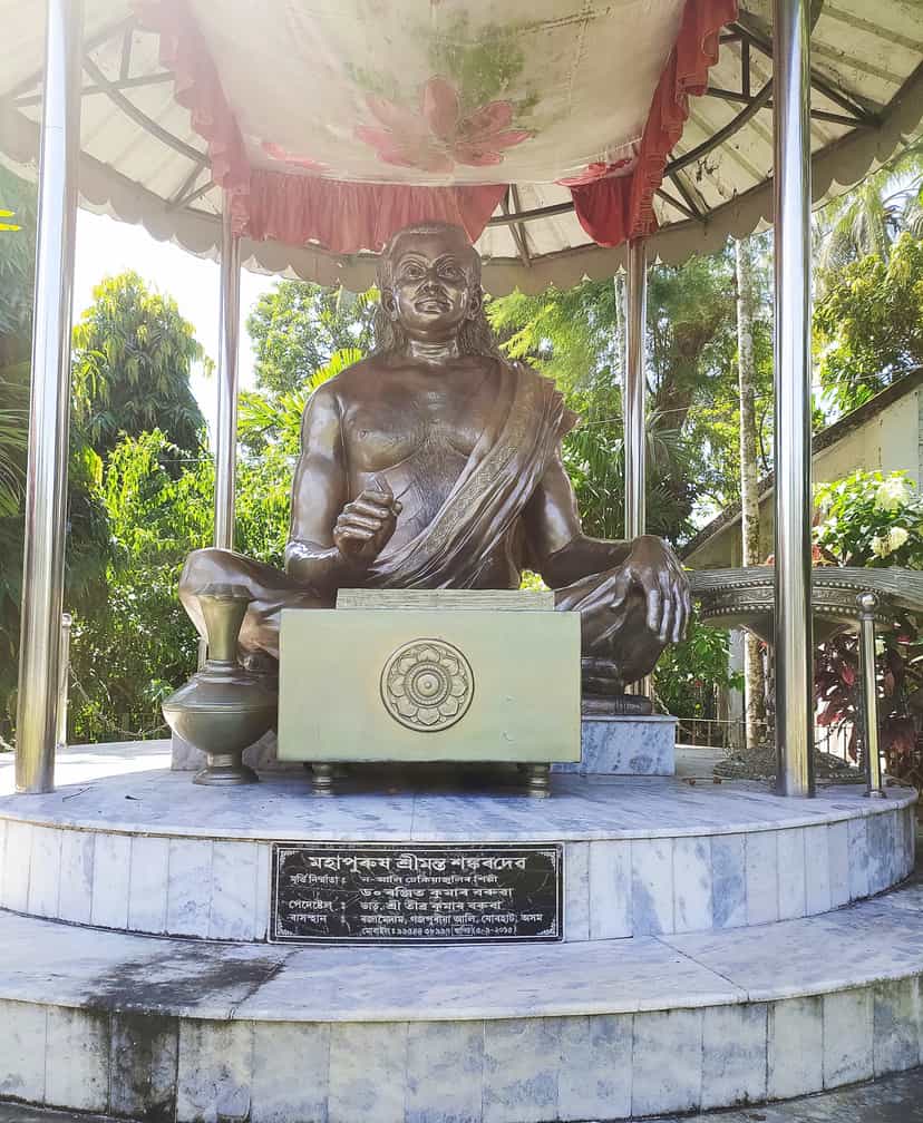 Seated bronze statue of Srimanta Sankardev beneath a canopy, with a dedicatory plaque naming the saint