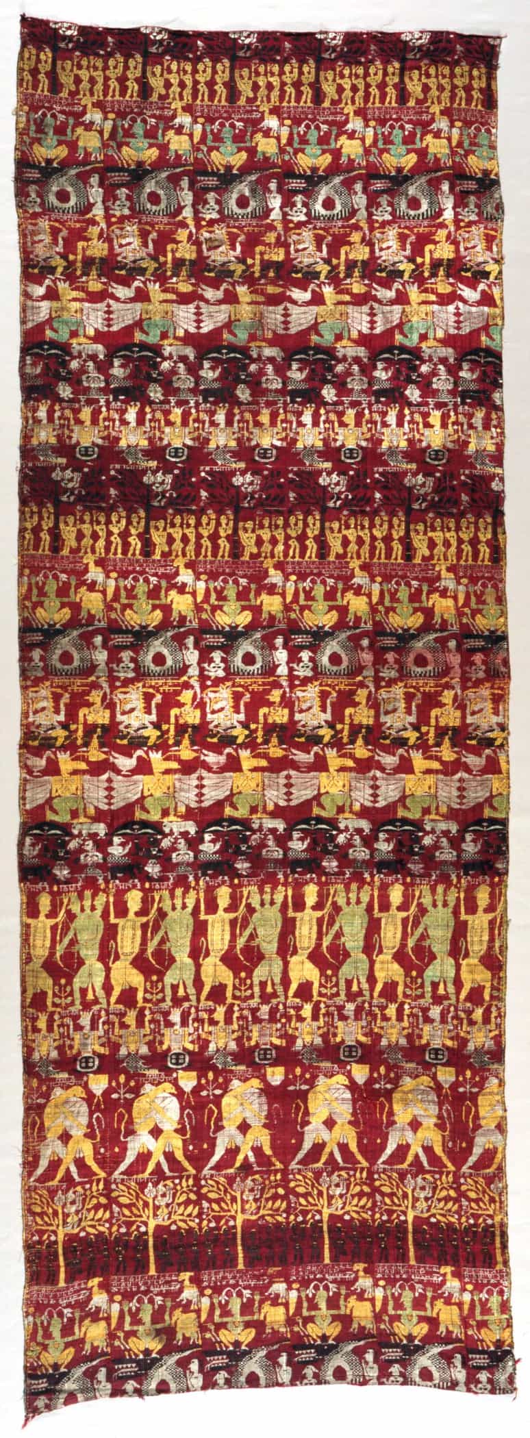 A woven silk panel in deep red, gold and cream showing rows of figures, dancers and elephants from the life of Krishna