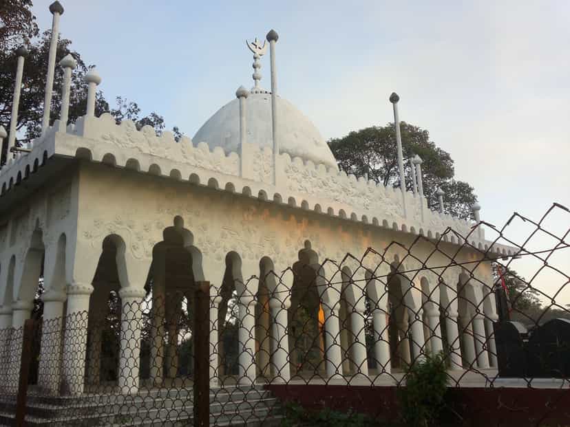 White domed shrine of Ajan Pir with floral-relief plasterwork and an arcaded verandah on the river island at Saraguri Chapori