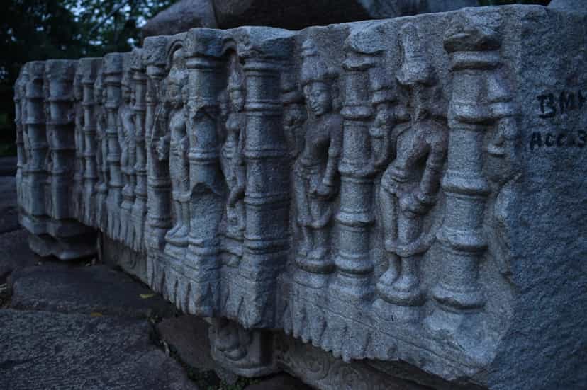 A long carved architectural member from the Bamuni Hills, a row of standing celestial figures alternating with turned colonnettes, the stone resting among the conserved fragments of the mound.