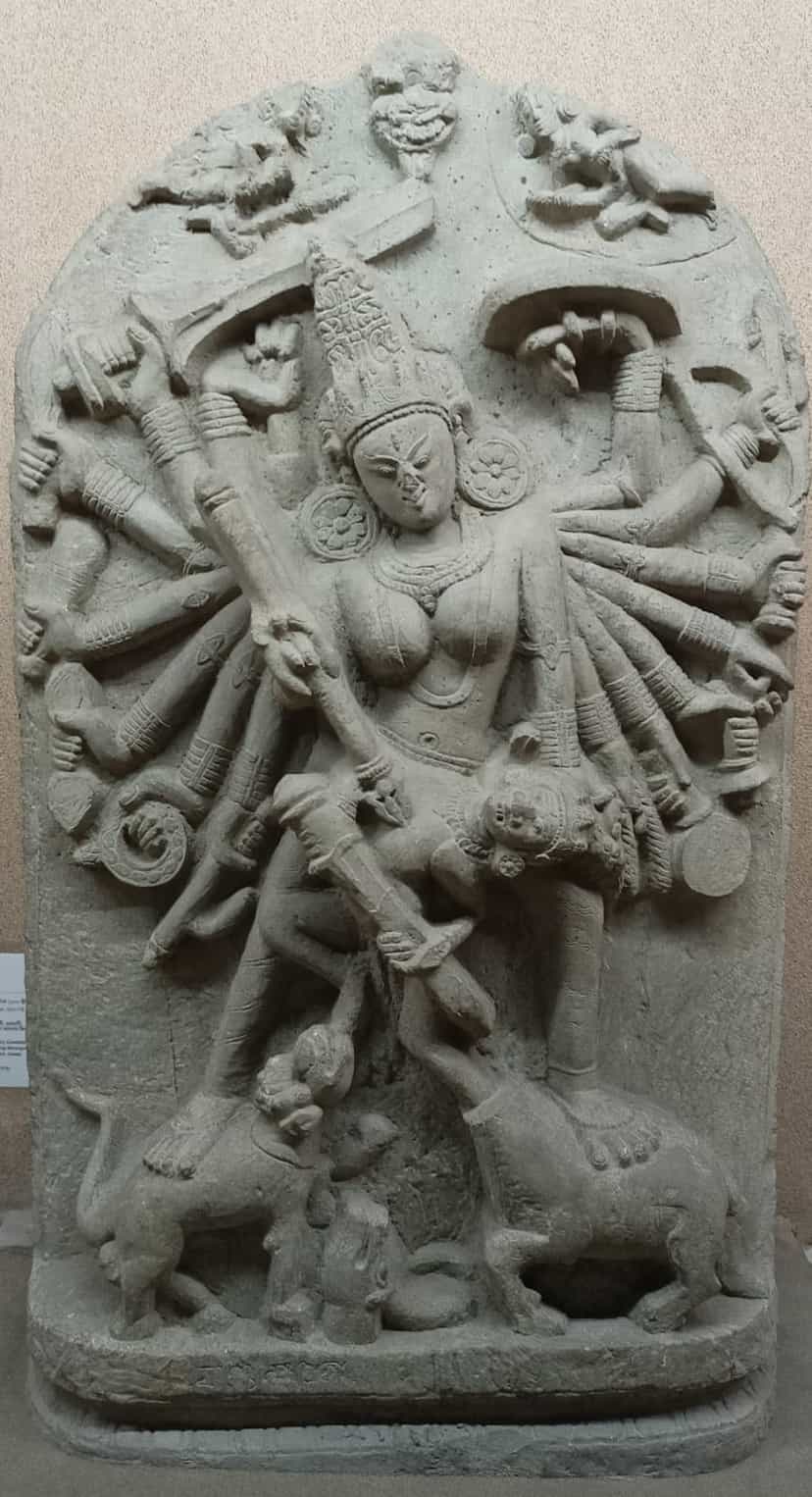 A grey stone stele of the many-armed goddess Durga slaying the buffalo demon, her lion and the demon figures at her feet