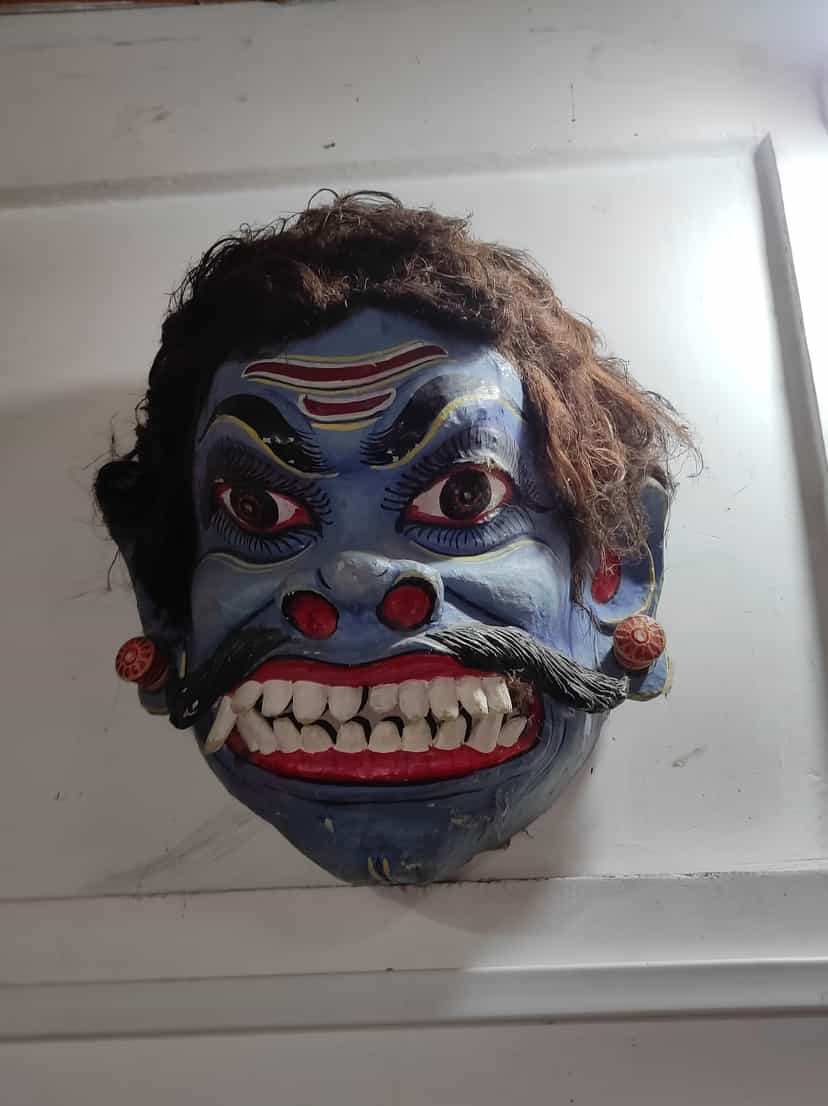 Blue-faced demon mukha with bulging eyes, bared white teeth, a thick black moustache and dark hair, a Majuli mask for a bhaona villain