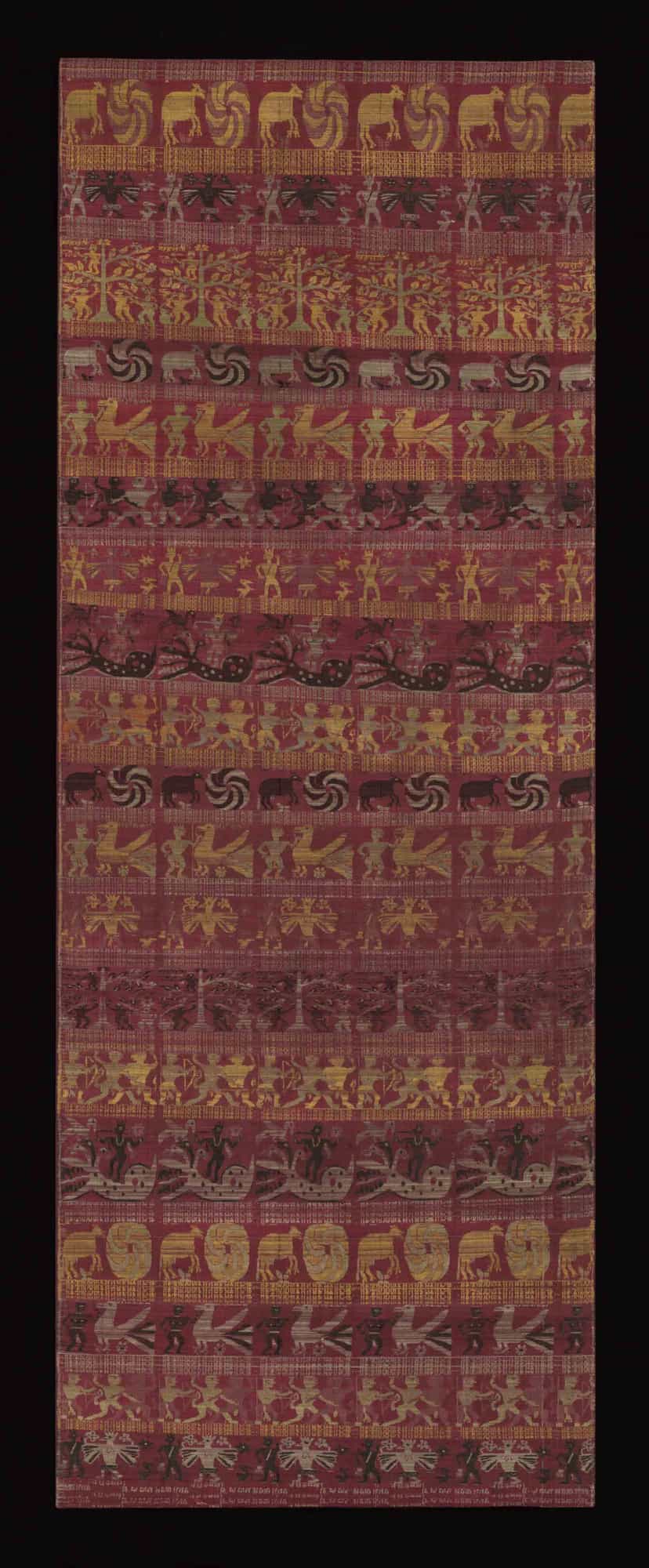 A long figured silk cloth from Assam woven in deep red, gold and black with horizontal registers of dancing figures, bulls, birds, trees of life and processional scenes