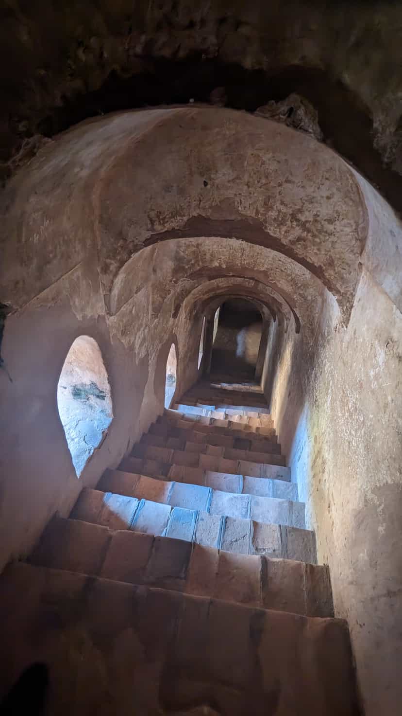 A vaulted brick staircase descending into the lower storeys of the Talatal Ghar, daylight falling from a side opening onto worn masonry steps