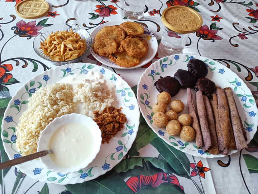 A Bihu spread of jolpan with curd, coconut laru balls, til pitha rolls and fried pithas on patterned plates