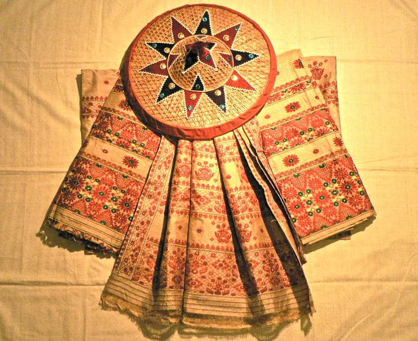 A length of golden muga silk mekhela-chador woven with red and gold floral and pictorial borders, laid out with a decorated japi