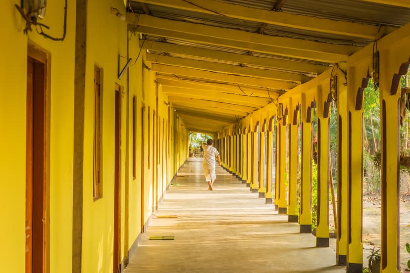 A long colonnade of yellow square pillars at Auniati Sattra receding to a bright vanishing point, a single distant figure walking down the shaded walkway