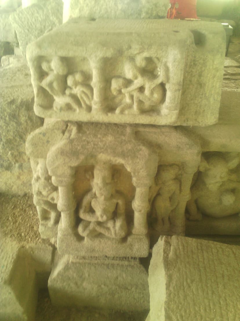 Two stacked carved sandstone blocks recovered at Madan Kamdev: the upper course bears a row of figural relief panels and the lower a small deity seated cross-legged within a pillared niche, with further carved fragments around them