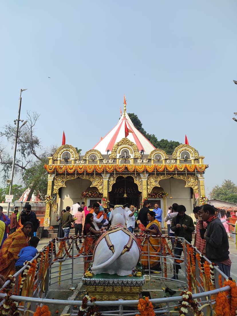 The Mahabhairab temple at Tezpur on a festival day, its gold-ornamented facade hung with marigold garlands beneath a red-and-white canopy and a tall white spire, devotees gathered around the Nandi shrine in front