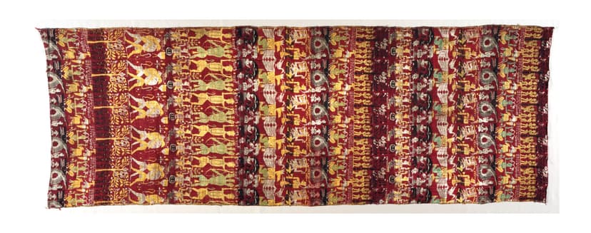 A woven silk panel in deep red, gold and cream showing rows of figures, dancers and elephants from the life of Krishna