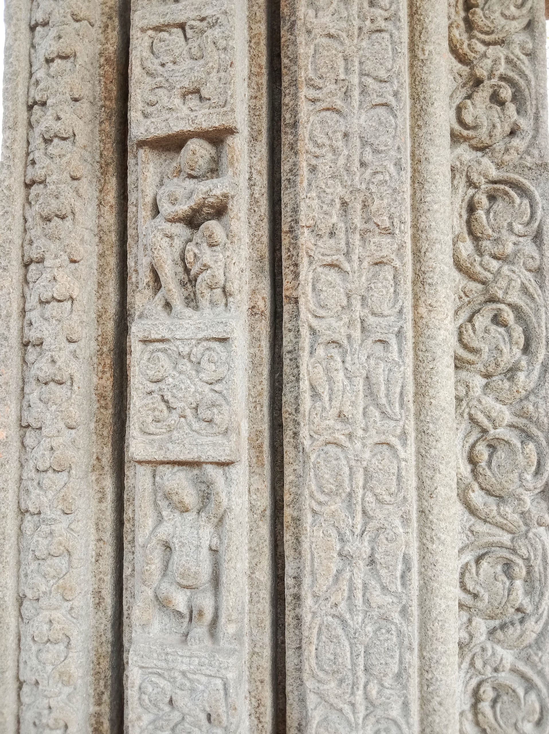 Close view of a carved stone door jamb at Da Parbatia, with bands of floral scrollwork flanking a narrow panel of small standing figures