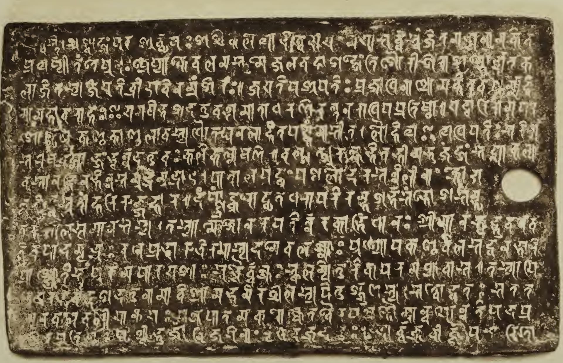 A dark copperplate photographed in 1897, fourteen lines of raised script and a ring hole at its right edge