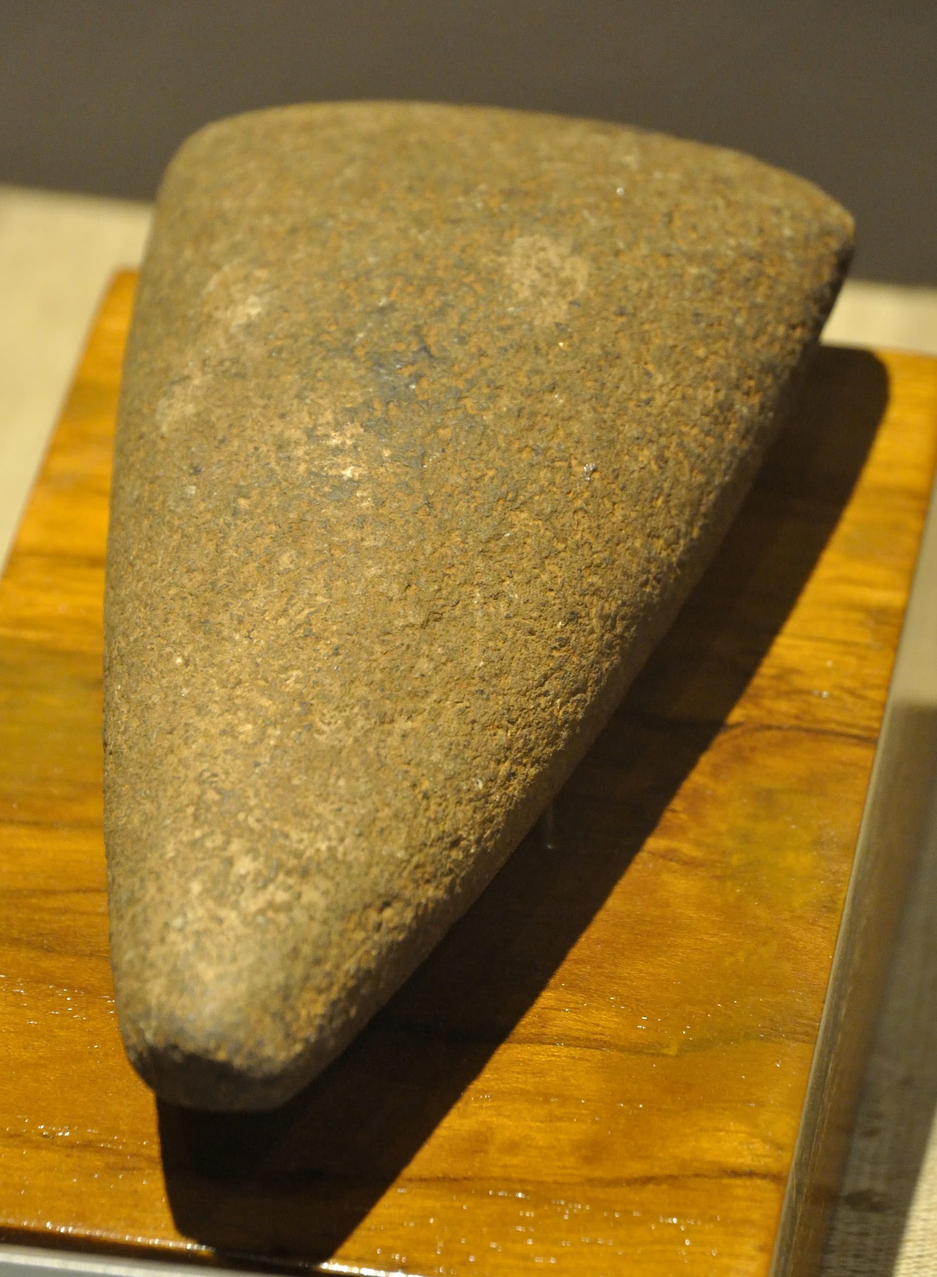 A polished triangular Neolithic stone celt mounted on a wooden museum stand