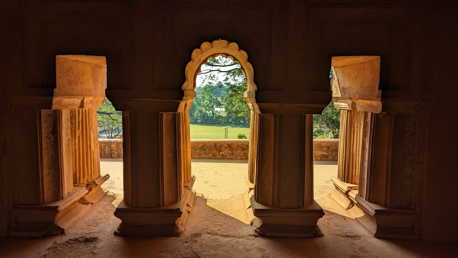 Cusped masonry archway inside the Kareng Ghar palace at Garhgaon, opening onto green grounds