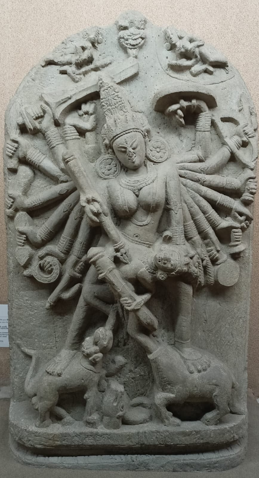 A grey stone stele of the many-armed goddess Durga slaying the buffalo demon, her lion and the demon figures at her feet