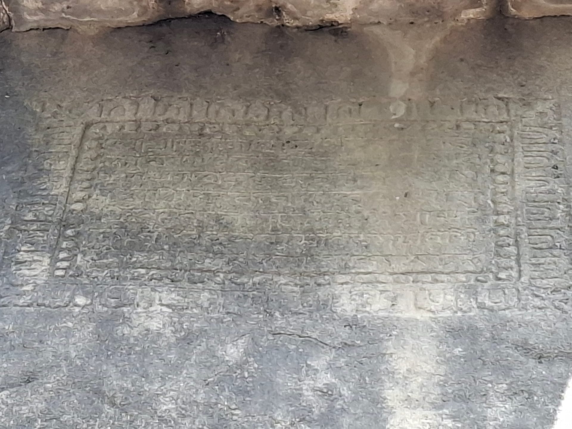 The rock-cut Kanai Boroxi inscription of 1205-06 CE, lines of old characters within a carved border on the granite