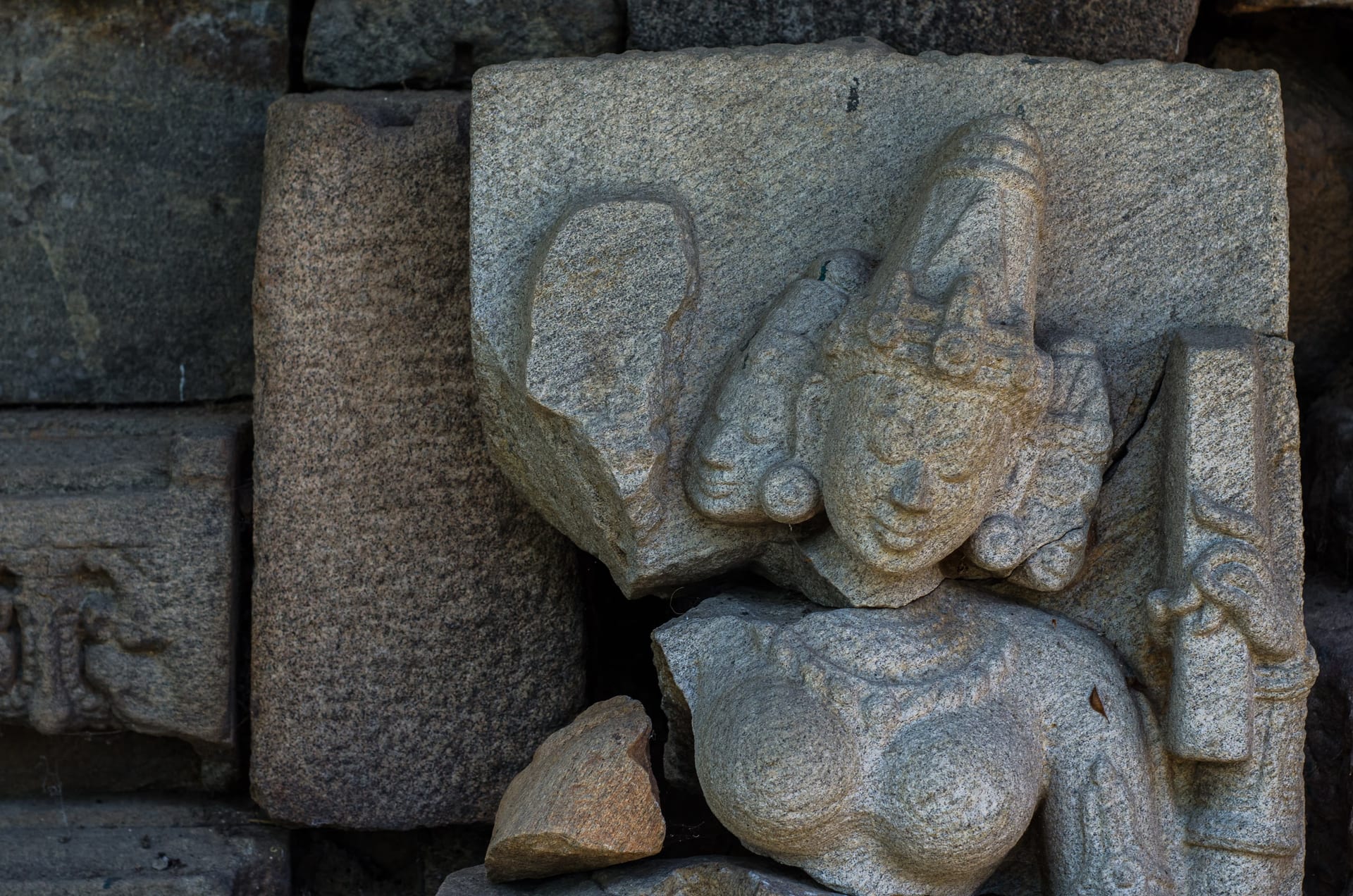 A Pala-period stone relief from Madan Kamdev seen close: a carved celestial female figure with a finely worked crowned face, jewellery and torso, warm raking light modelling the dense carving against the surrounding recovered stone blocks