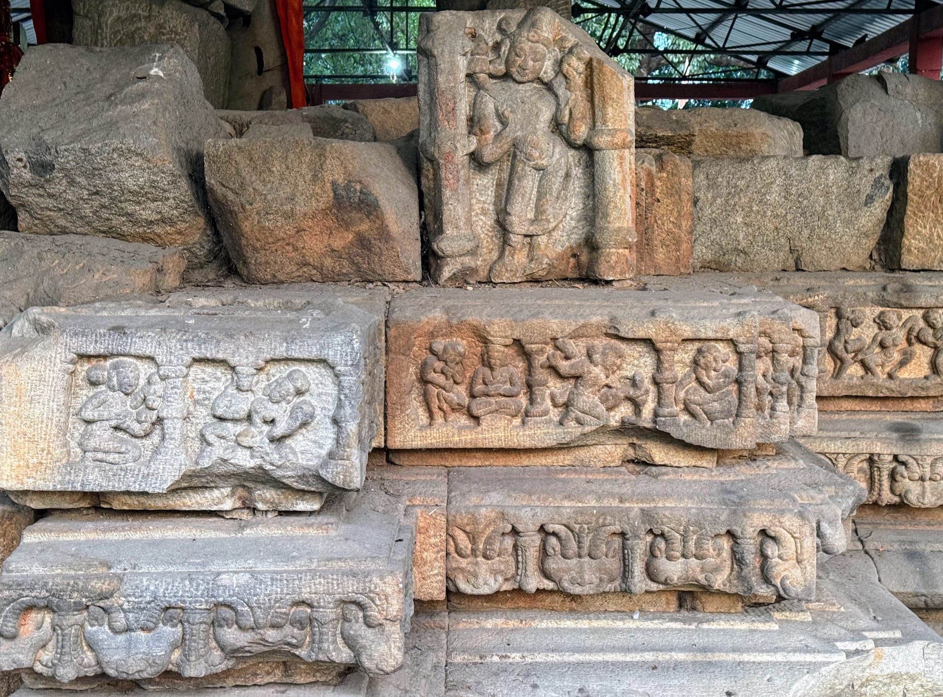 A standing carved deity in a pillared niche on stacked stone, with rows of small gana figures carved in the courses below