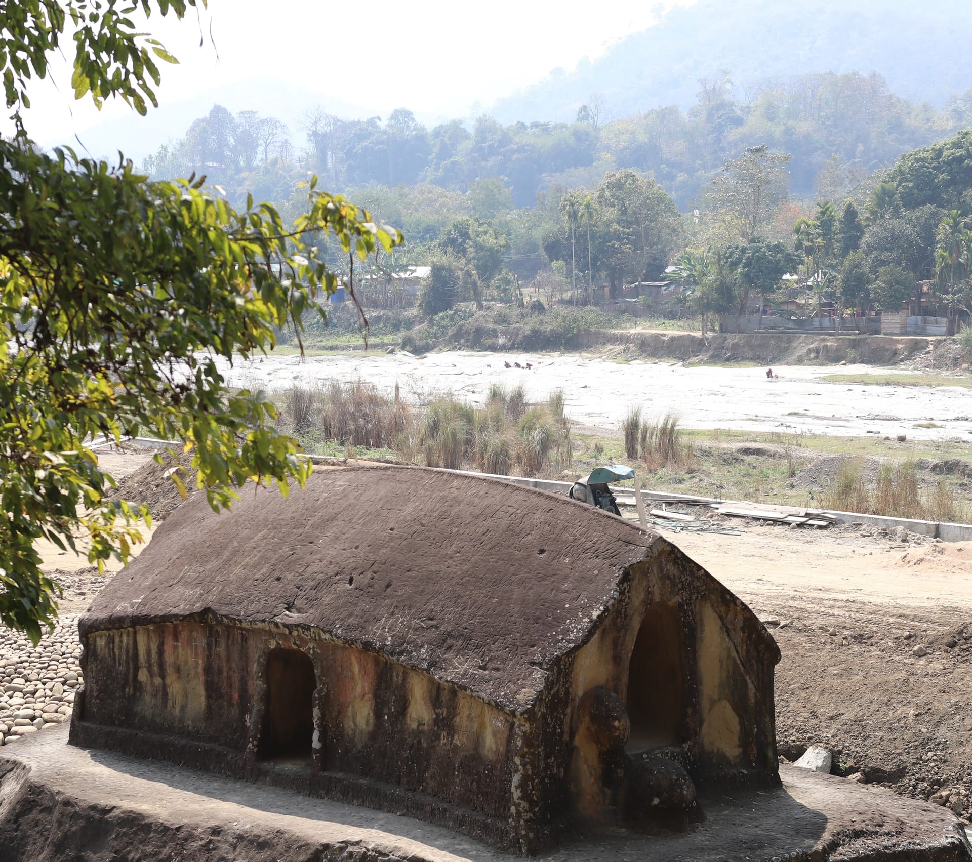 The Maibang Stone House, a low stone temple with arched openings standing on the bank of the Mahur river, hills rising behind