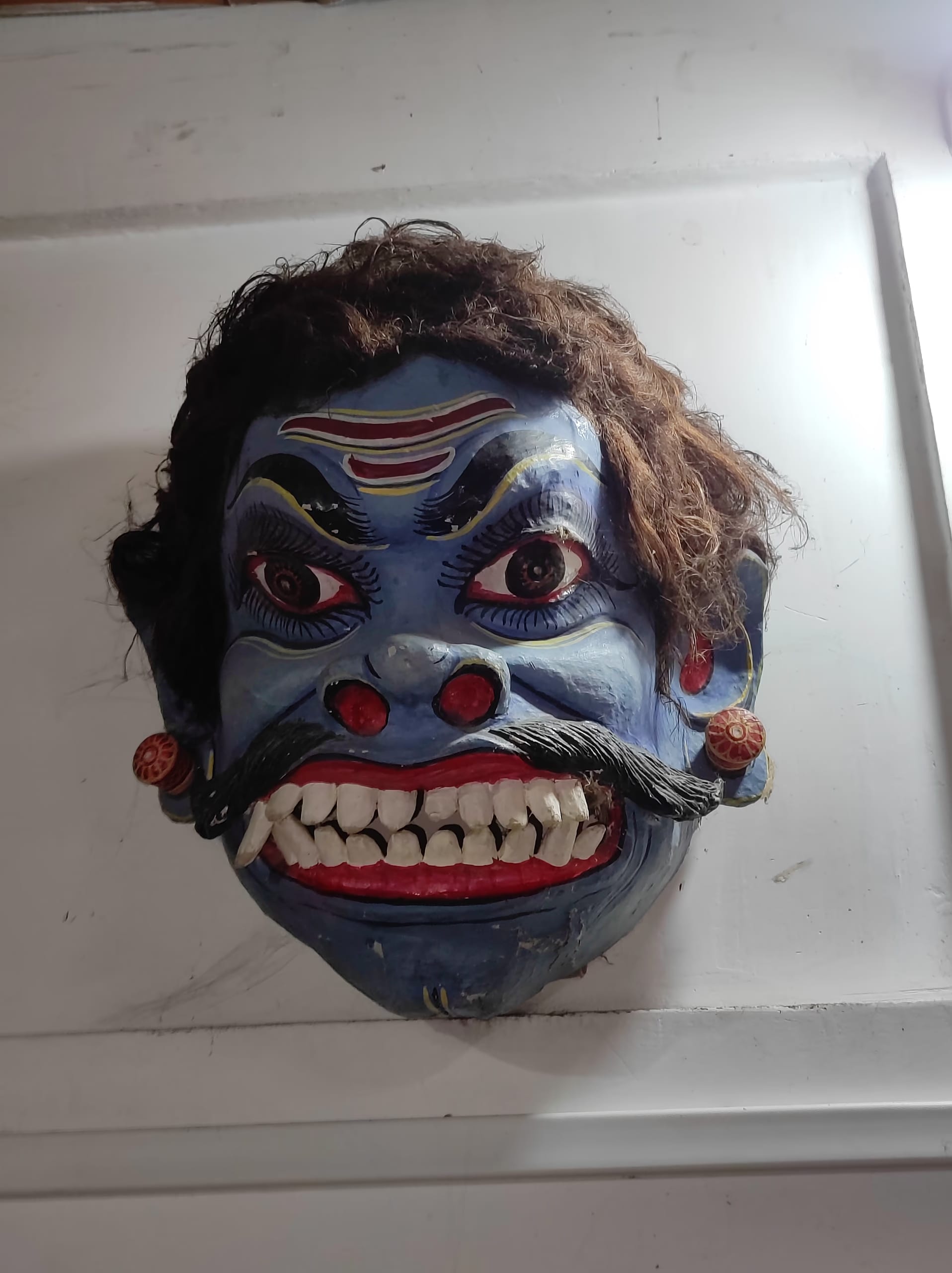 Blue-faced demon mukha with bulging eyes, bared white teeth, a thick black moustache and dark hair, a Majuli mask for a bhaona villain