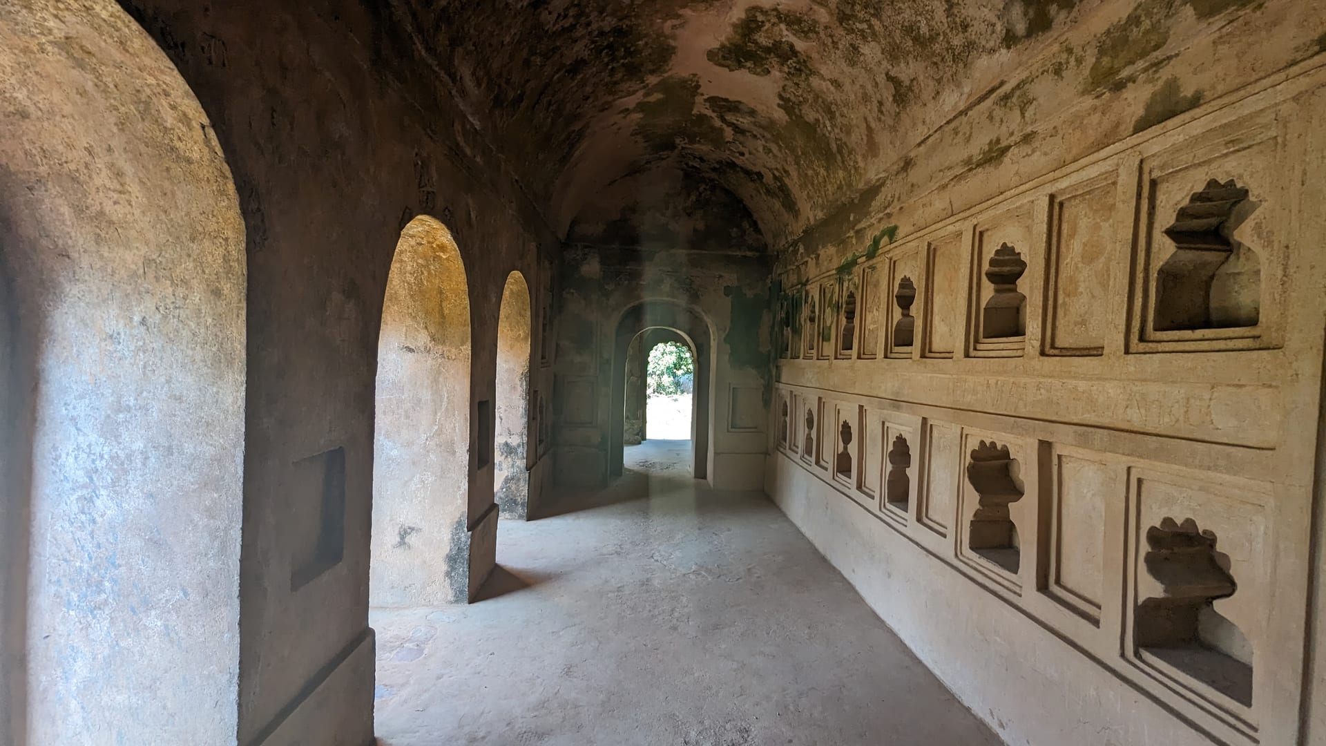 A vaulted brick corridor inside the Talatal Ghar, arched openings along one wall and carved plaster niches along the other