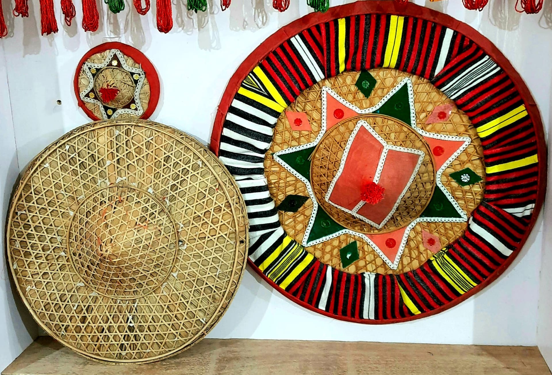 An undecorated bamboo japi beside two japis covered in red, green and white cloth with star appliqué