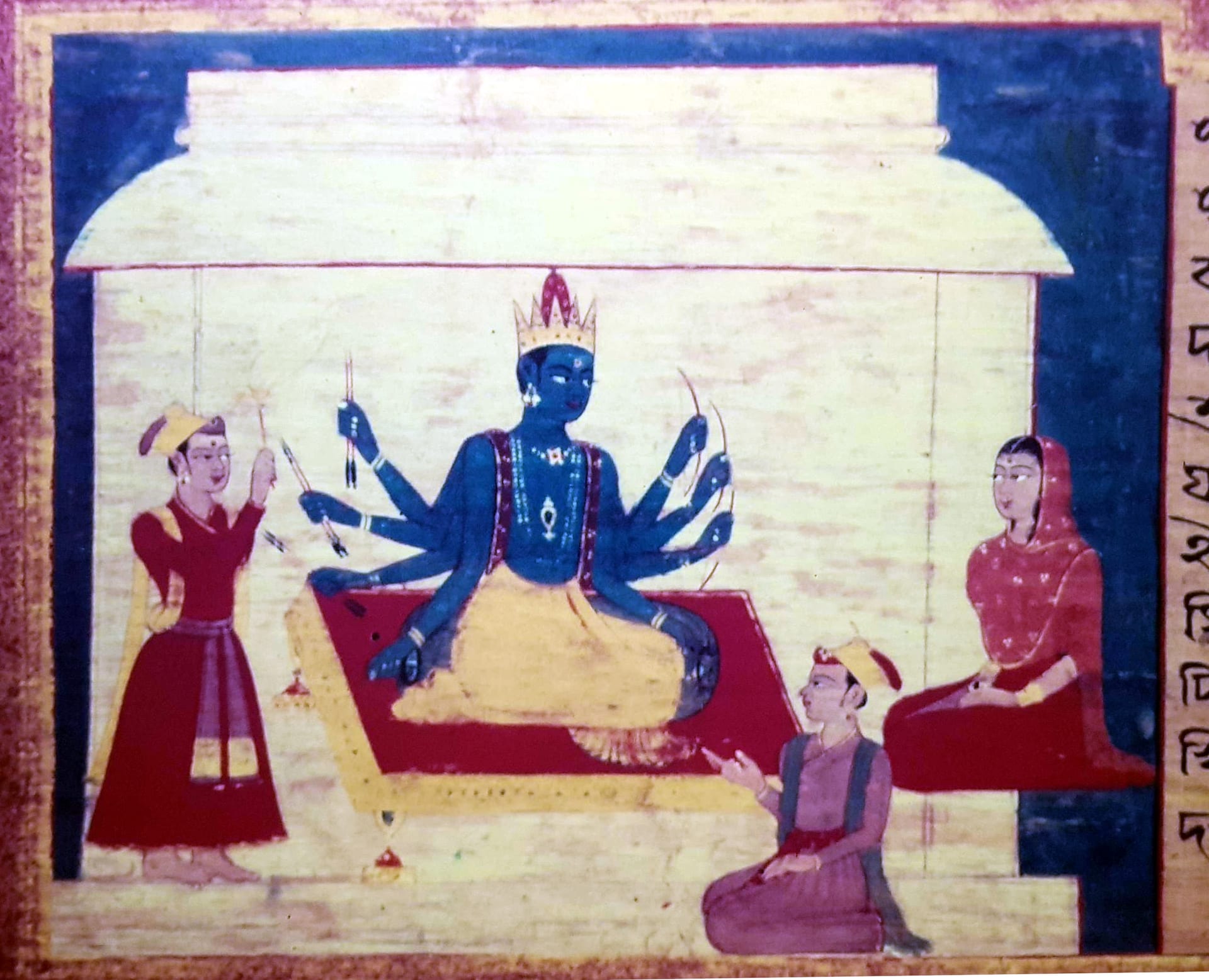 An Assamese manuscript painting: a blue, many-armed crowned deity seated on a red dais under a pavilion, an attendant offering at left and a seated woman at right, a column of old Assamese script running down the right edge