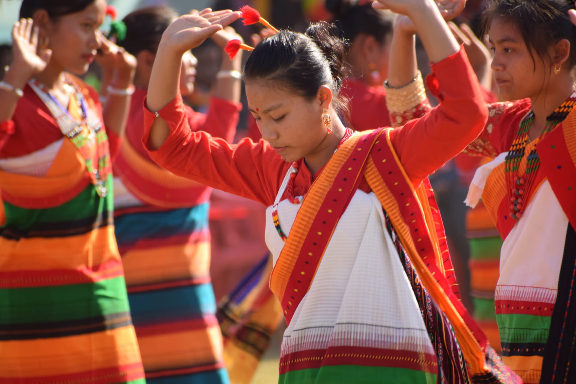 Dimasa women in striped wraps dancing with arms raised