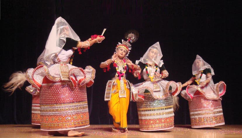 Manipuri Ras Lila dancers: a central figure costumed as Krishna with a flute, flanked by three gopis in the stiff, mirror-worked cylindrical Kumil skirt and translucent white veil