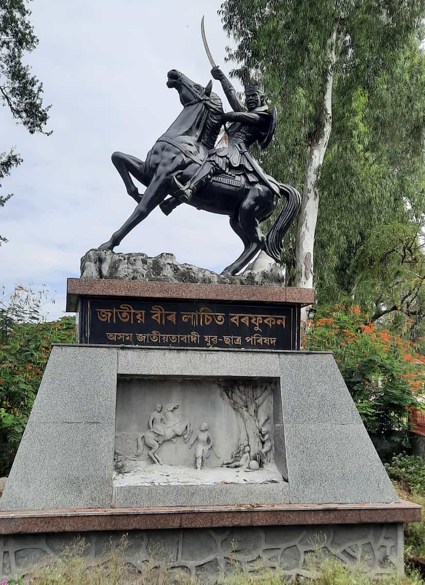 Black equestrian statue of Lachit Borphukan brandishing a curved sword astride a rearing horse, on a granite pedestal inscribed in Assamese with a carved relief panel below