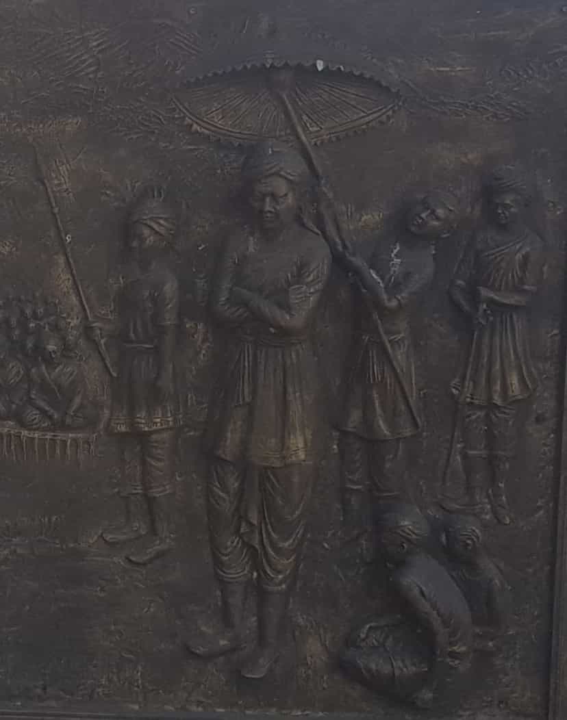 Bronze relief panel of Momai Tamuli Borbarua, the first Borbarua, standing beneath a ceremonial parasol with attendants