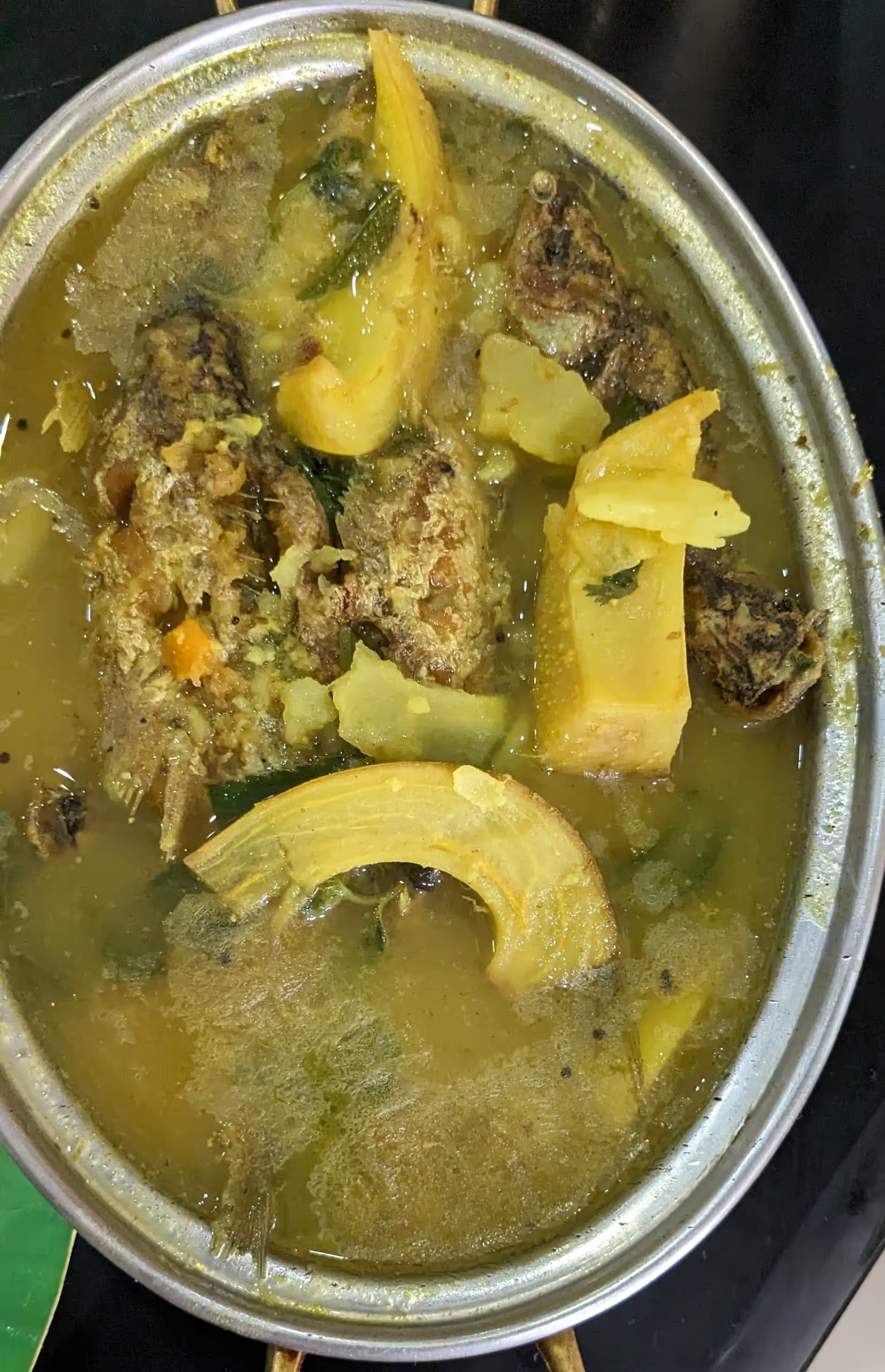 A bowl of fish curry with pieces of pale yellow elephant-apple, seen from above