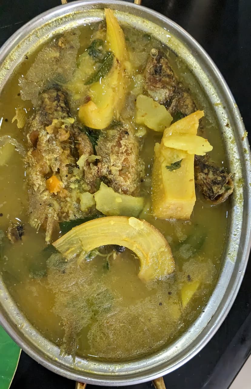 A bowl of fish curry with pieces of pale yellow elephant-apple, seen from above