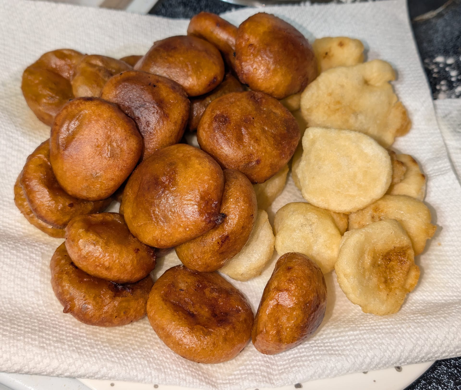 A pile of deep golden-brown, knee-shaped fried rice cakes beside paler fried rice pieces on a paper towel