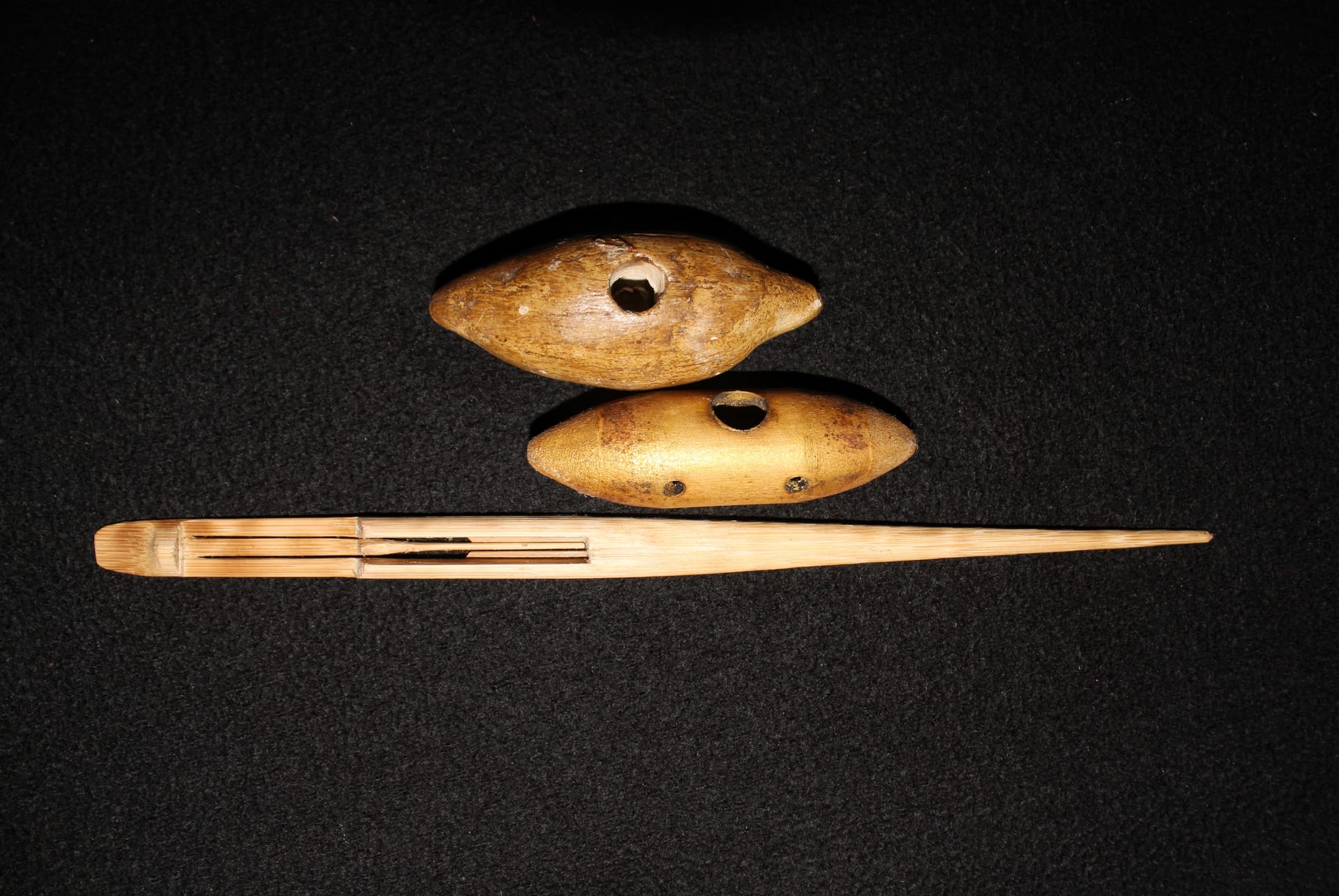 A bamboo gogona jaw harp with a long split tongue laid beside two small oval xutuli whistles on a dark cloth