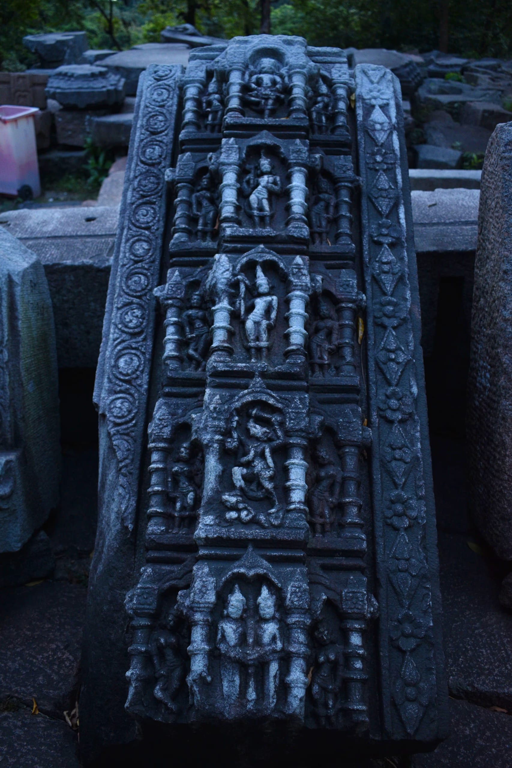 A tall carved stone panel from the Bamuni Hills, divided into stacked registers, each niche framed by colonnettes and holding a standing figure, with decorative roundels and floral motifs down the sides.