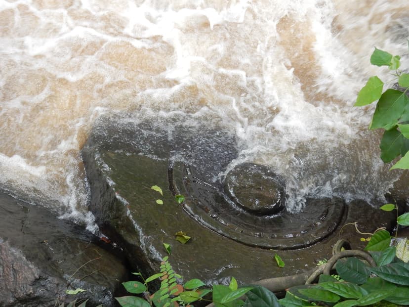 A Shiva lingam and its circular yoni carved into the dark bedrock of a stream, with white water rushing over it