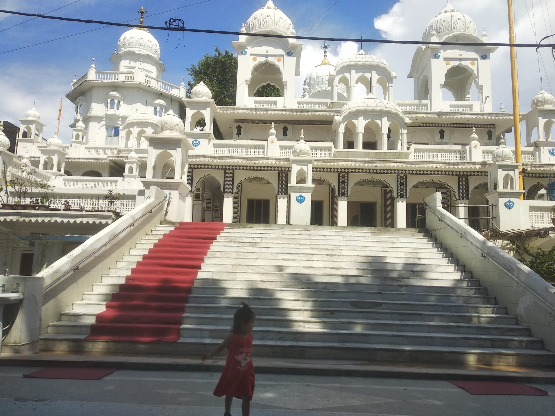 Frontal view of the white marble Gurudwara Damdama Sahib at Dhubri, its many domes and chhatris above a broad red-carpeted staircase under a blue sky