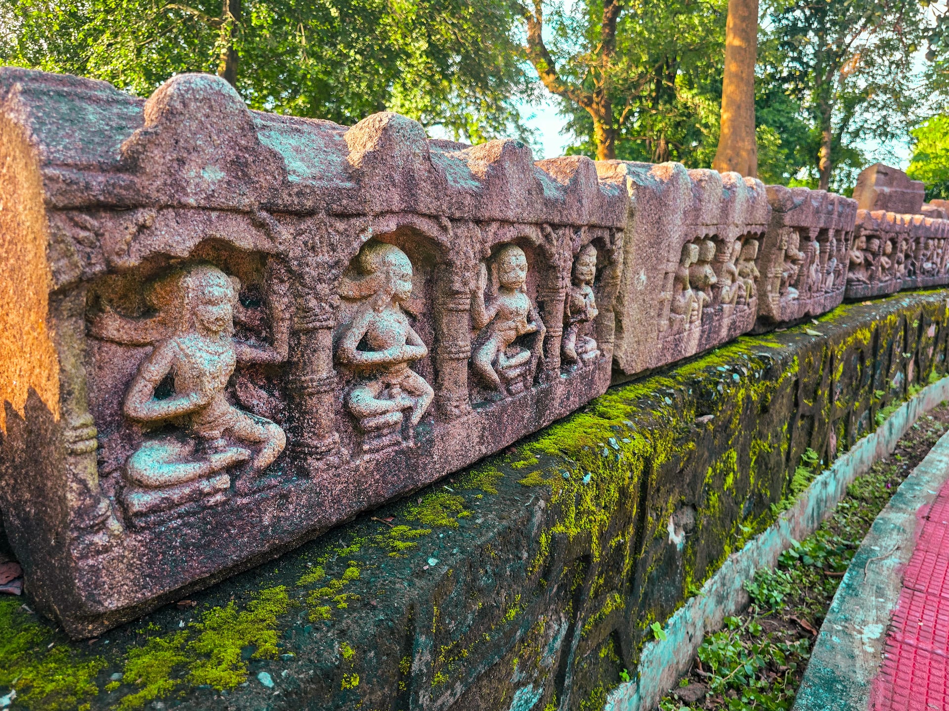 A long row of carved stone panels with seated figures set in arched niches at Deopahar