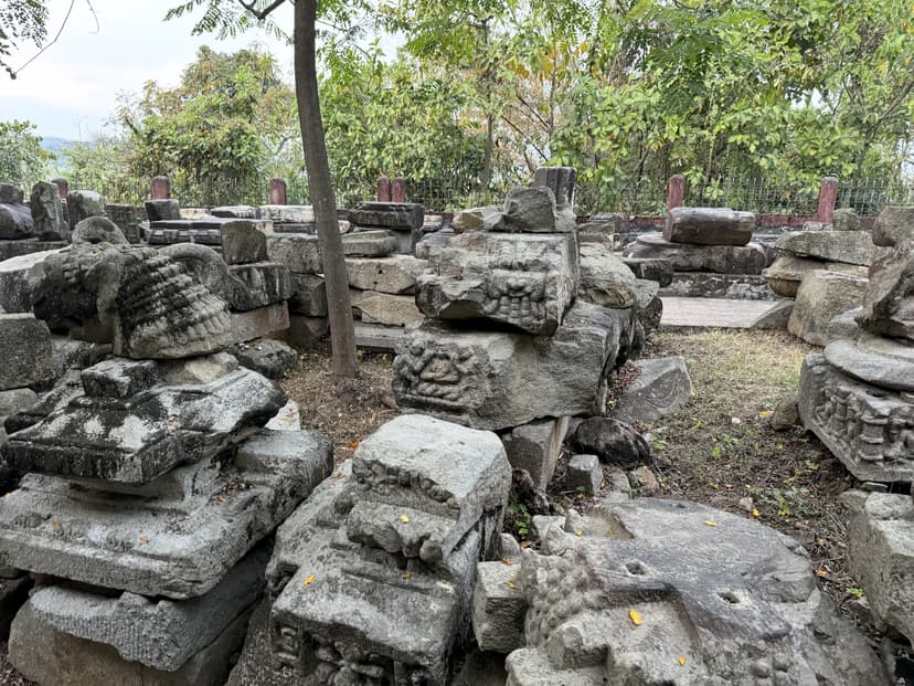 A wide field of scattered carved granite blocks, plinths and mouldings among trees at Madan Kamdev