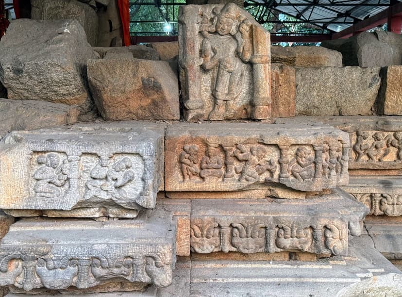 A standing carved deity in a pillared niche on stacked stone, with rows of small gana figures carved in the courses below