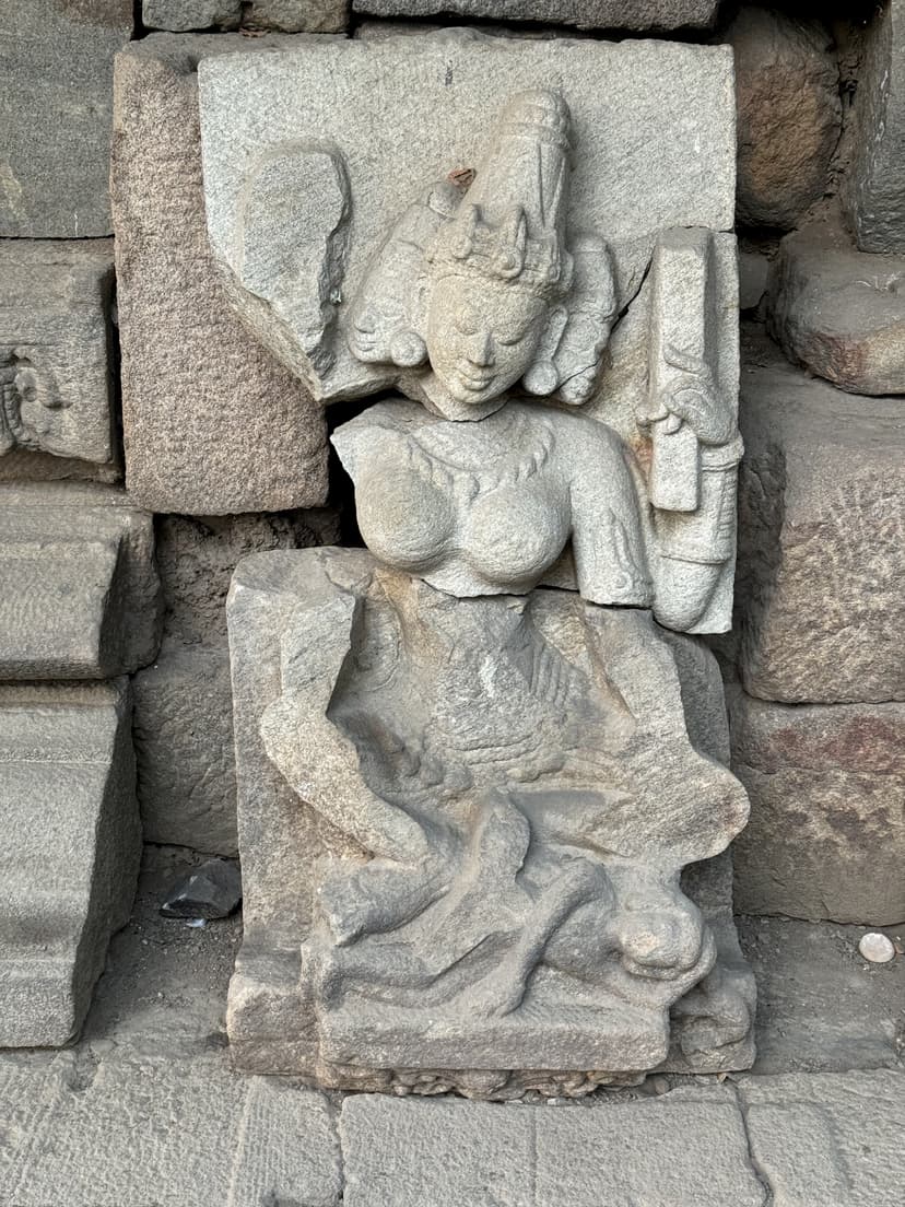 A finely carved crowned female figure in stone with elaborate headdress and jewellery among stacked temple blocks
