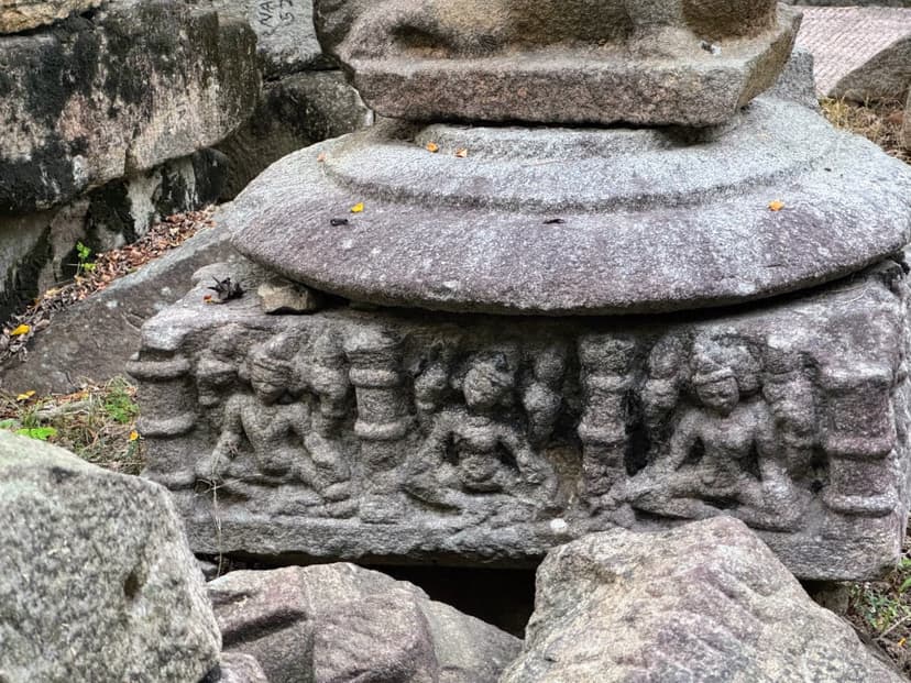 Weathered stone block with three seated multi-headed deities in niches at Madan Kamdev