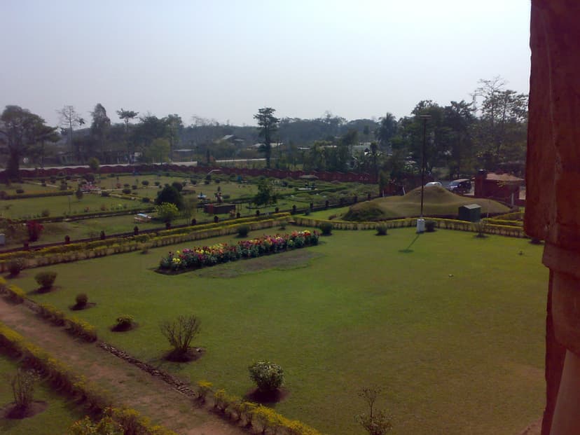 View looking down from the upper gallery of the Rang Ghar over the landscaped gardens, with geometric flower beds, clipped hedges, an open lawn and a tree line beyond