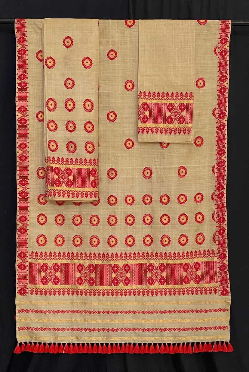 A two-piece muga silk mekhela-sador laid on a black ground, its natural golden cloth worked with rows of red sunflower-like medallions and broad red-and-gold patterned borders