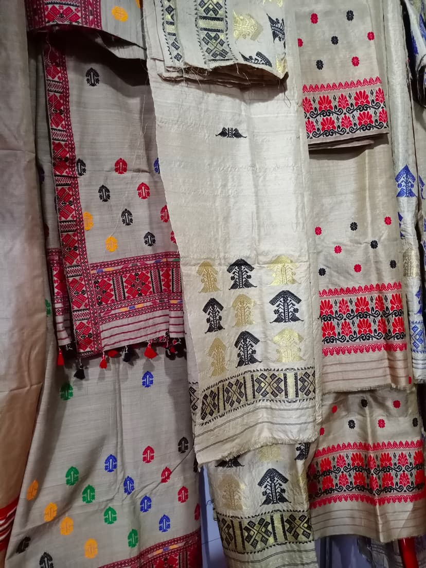 Several muga silk mekhela sador drapes with golden ground and red, black and coloured woven motifs hung on display