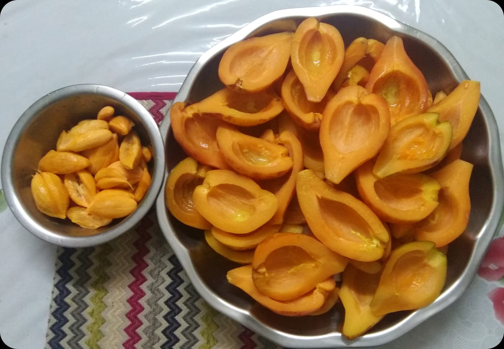 Halved bright-orange thekera fruit arranged in a metal bowl with separated seeds in a smaller bowl