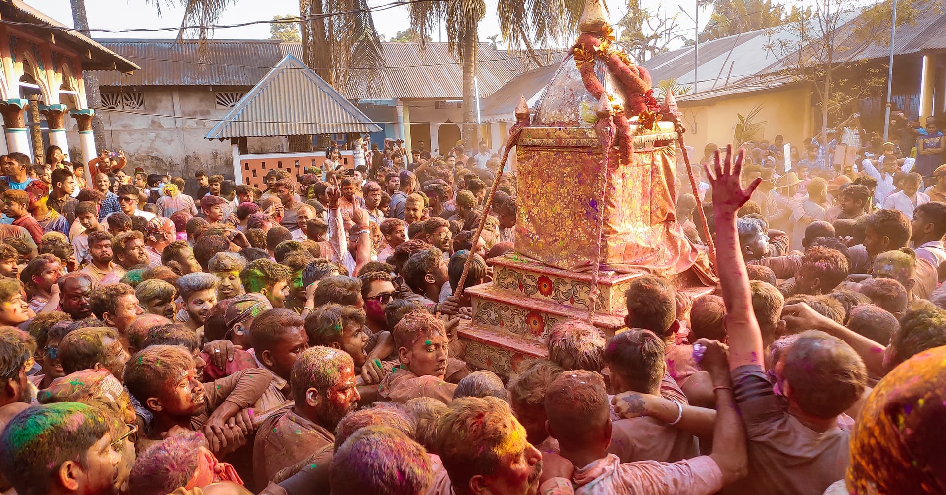 A colour-smeared crowd packs the Barpeta Sattra courtyard around the deity's palanquin during the phakuwa play of Doul Utsav