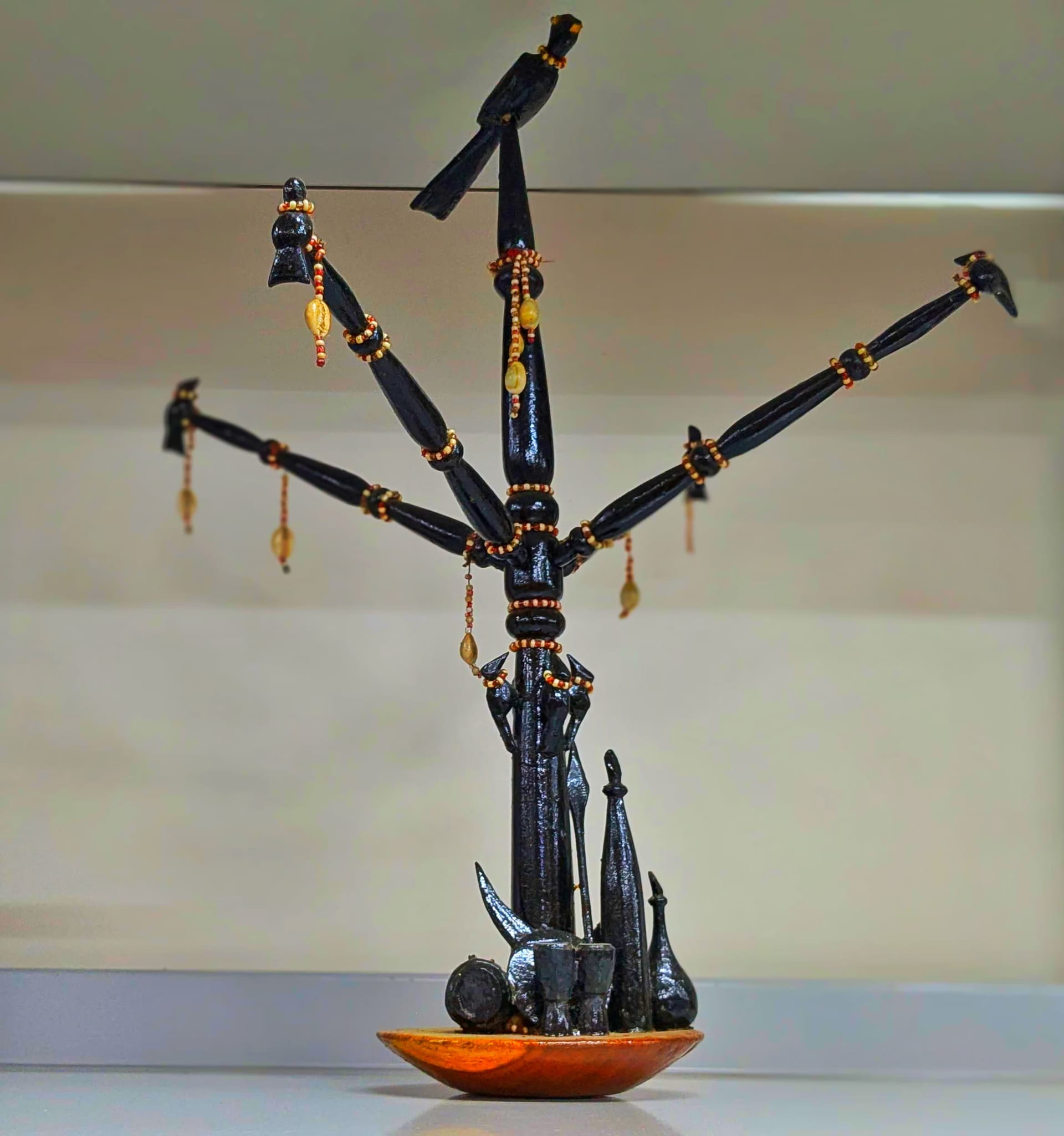 Carved black wooden totem with a central post and lateral branches, each tipped with a carved bird, mounted on a wooden dish