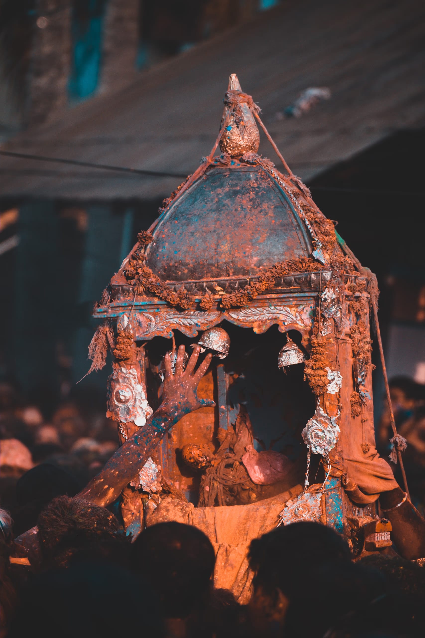A gulal-smeared palanquin carried above a crowd during the Doul festival at Barpeta